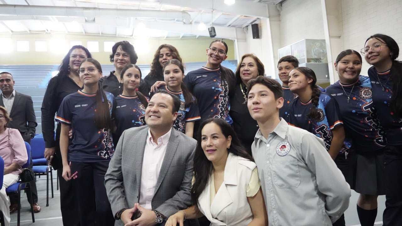 Estudiantes y personas adultas posan en grupo dentro de un gimnasio escolar.